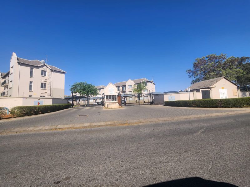 Front entrance view of the apartment complex featuring a secure gated access point, guard house, and paved driveway.