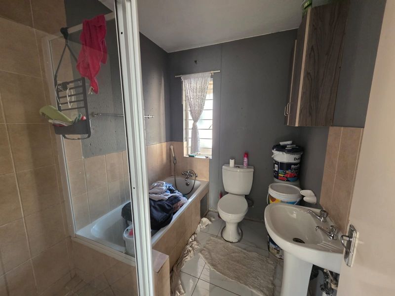 A functional bathroom featuring a bathtub, pedestal basin, and toilet, with tiled finishes and wall-mounted storage cabinetry.