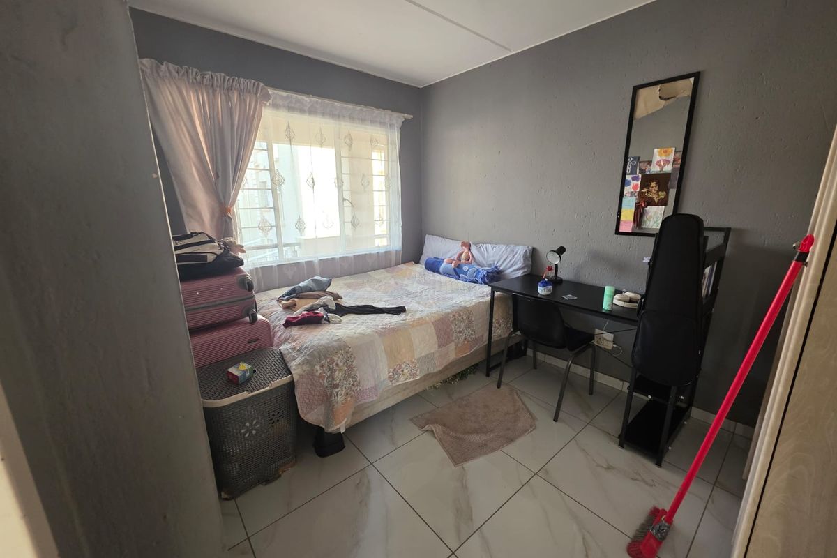 A compact bedroom featuring tiled flooring and a window fitted with security bars, offering a functional living space.