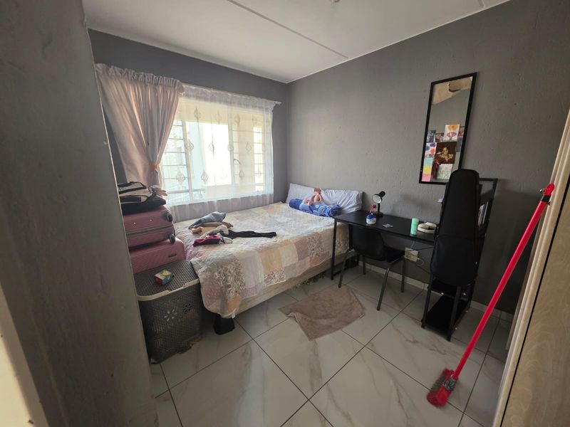 A compact bedroom featuring tiled flooring and a window fitted with security bars, offering a functional living space.
