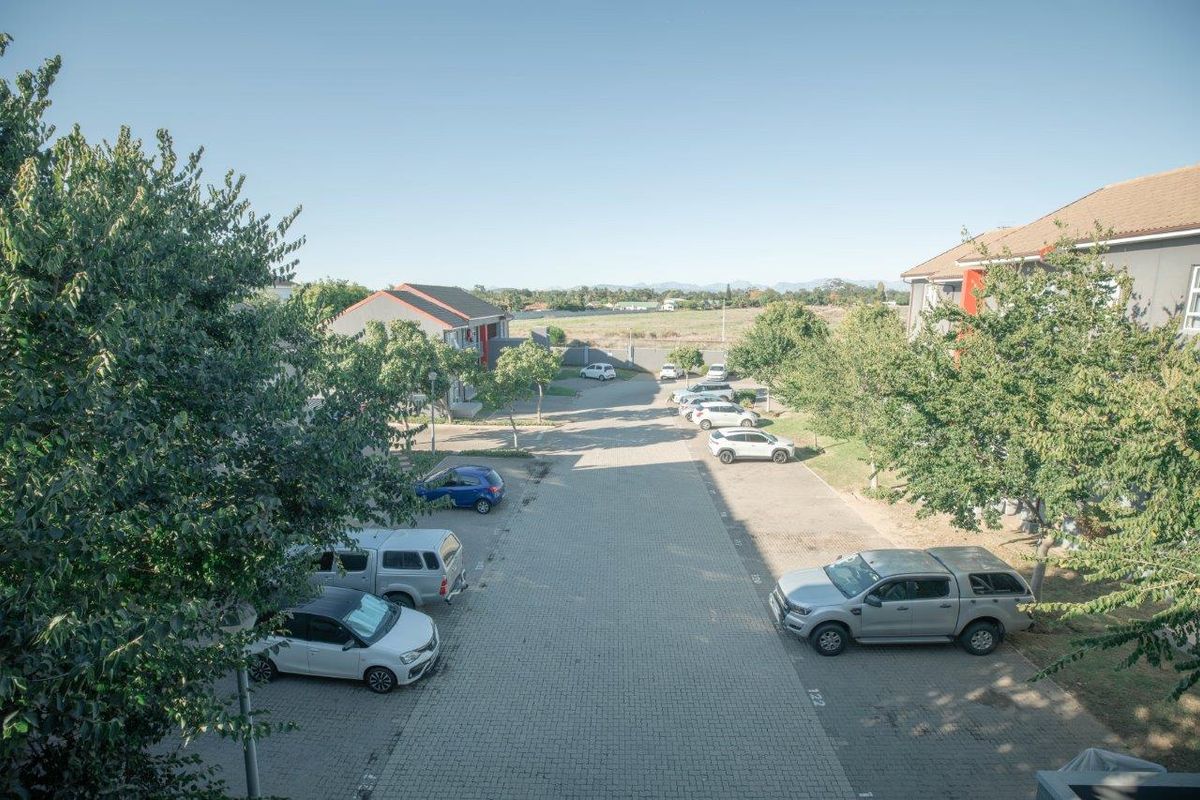 Elevated view of the apartment complex parking area, featuring paved driveways and established trees within the residential estate grounds.