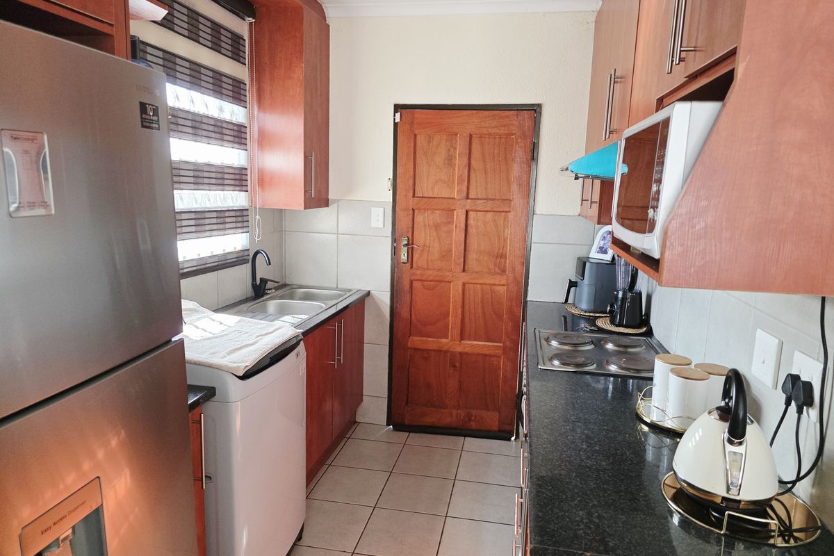 A functional kitchen featuring laminate cabinetry, granite countertops, an electric hob, built-in microwave, and tiled flooring with a timber door access.