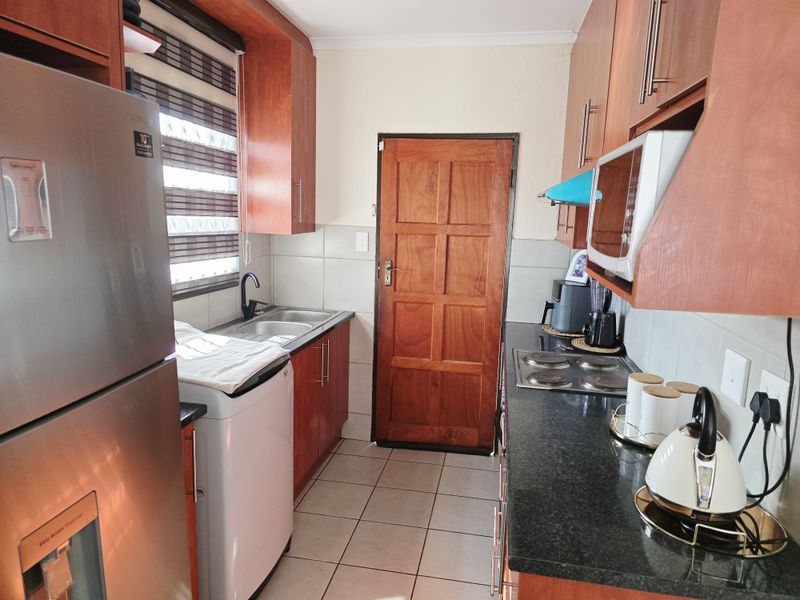 A functional kitchen featuring laminate cabinetry, granite countertops, an electric hob, built-in microwave, and tiled flooring with a timber door access.