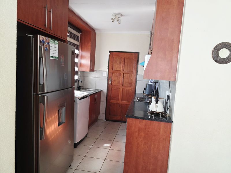 A functional kitchen featuring wood-finish cabinetry, granite countertops, tiled flooring, and a tiled splashback, providing a practical workspace.