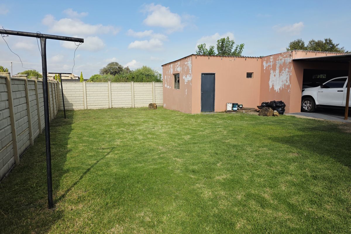 Rear garden area featuring a lawn, precast concrete boundary wall, and a carport with visible exterior paint deterioration on the adjacent structure.