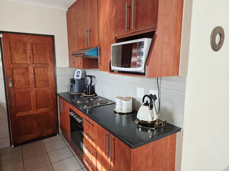 A functional kitchen featuring warm-toned wooden cabinetry, granite countertops, a built-in oven, electric hob, and a tiled backsplash.
