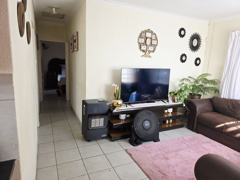A living room area featuring tiled flooring and coved ceilings, with a view leading into an adjacent hallway and bedroom.
