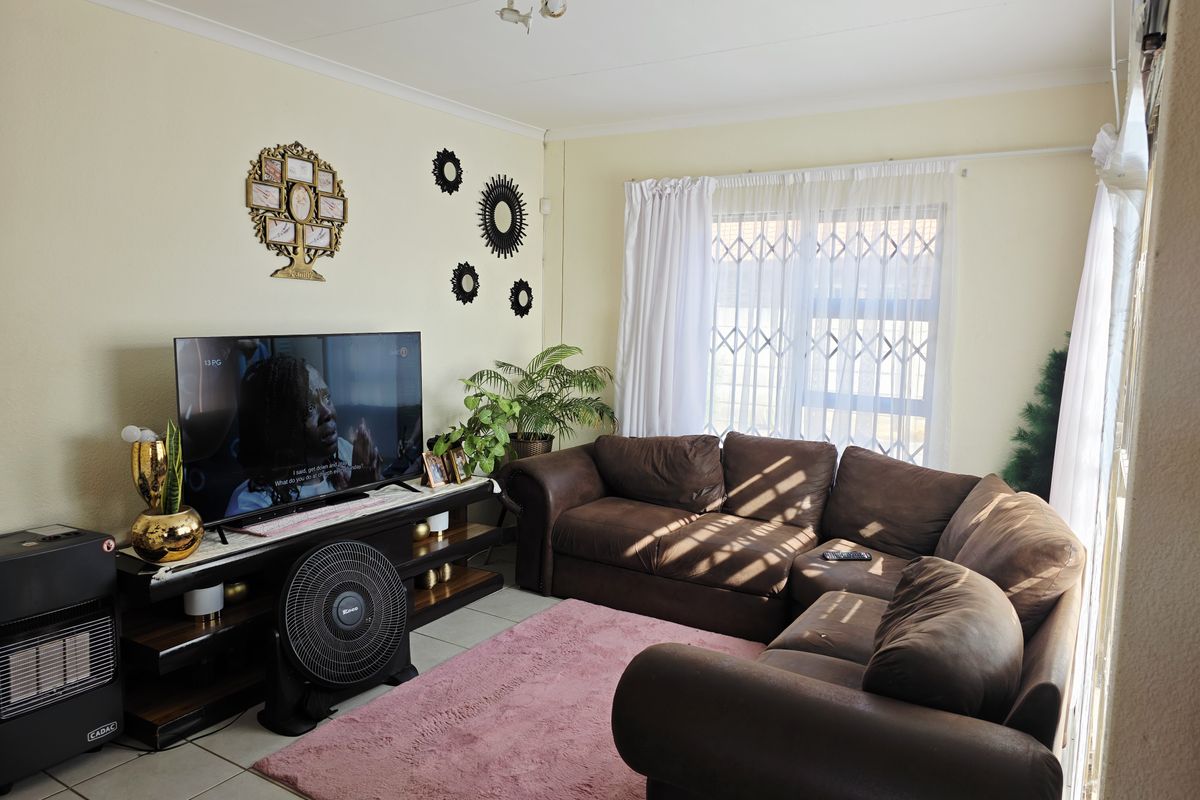 A comfortable living room featuring tiled flooring, a security gate on the window, and neutral wall finishes.