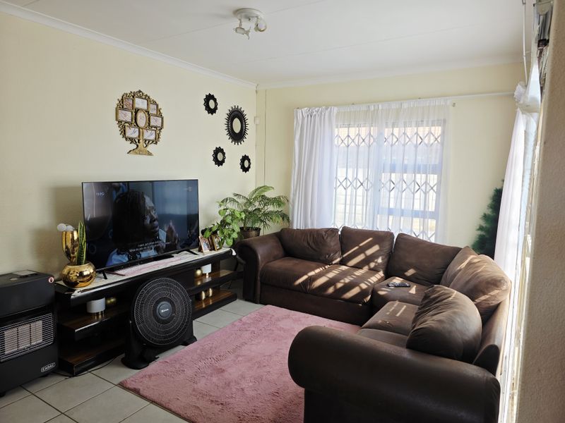 A comfortable living room featuring tiled flooring, a security gate on the window, and neutral wall finishes.