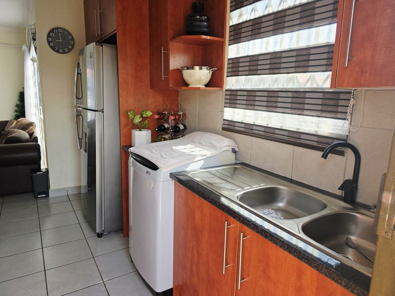 A functional kitchen area featuring warm-toned built-in cabinetry, granite countertops, a double stainless steel sink with a modern black tap, and tiled flooring.