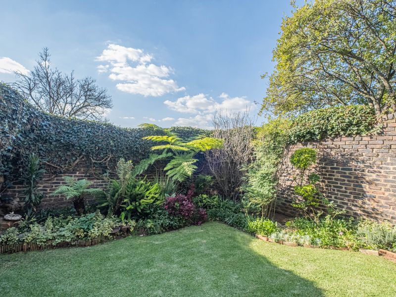 A well-maintained private garden featuring established greenery, lush lawn, and classic brick boundary walls providing a secluded outdoor space.