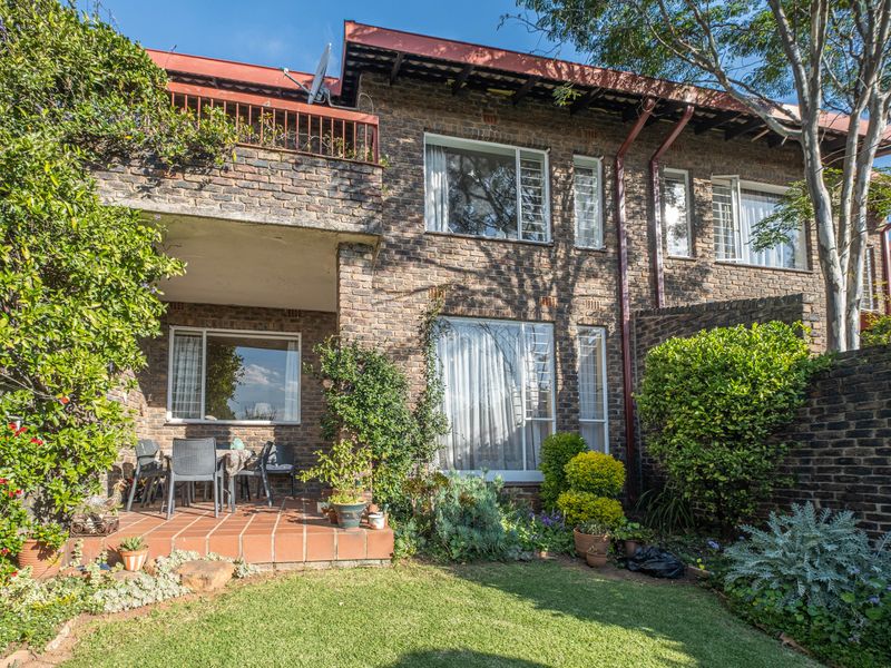 Rear view of a double-story townhouse featuring a face brick facade, a covered patio area, an upper-level balcony, and a well-maintained private garden.