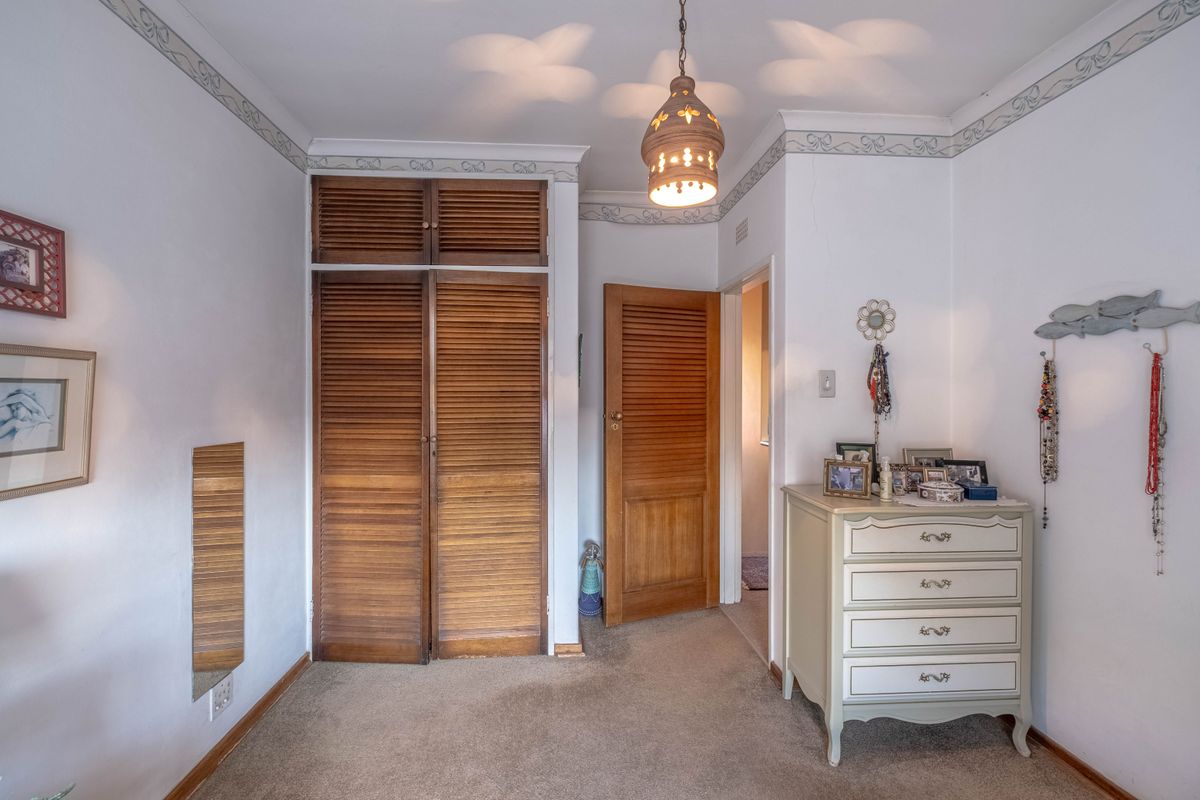 A bedroom featuring built-in wooden louvered wardrobes, carpeted flooring, and decorative wall detailing, offering a functional space with classic finishes.