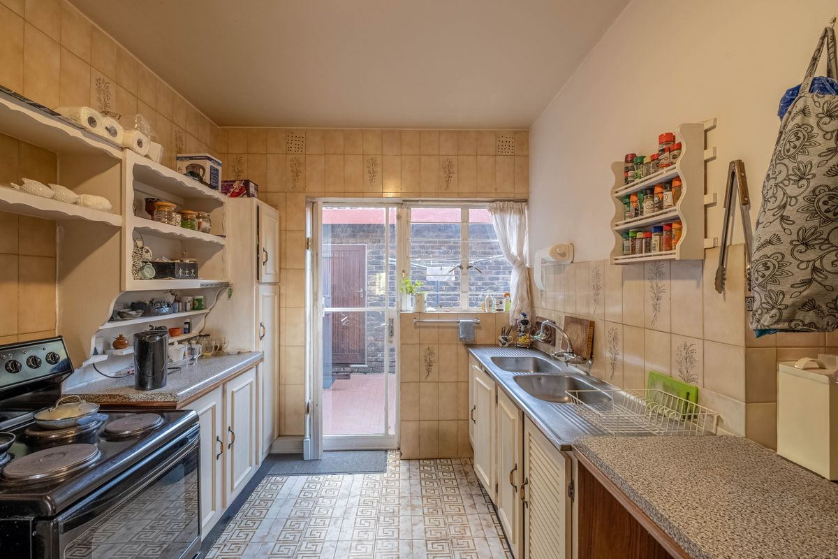 A functional kitchen featuring dated cabinetry, laminate countertops, a double stainless steel sink, and direct access to an exterior courtyard area.