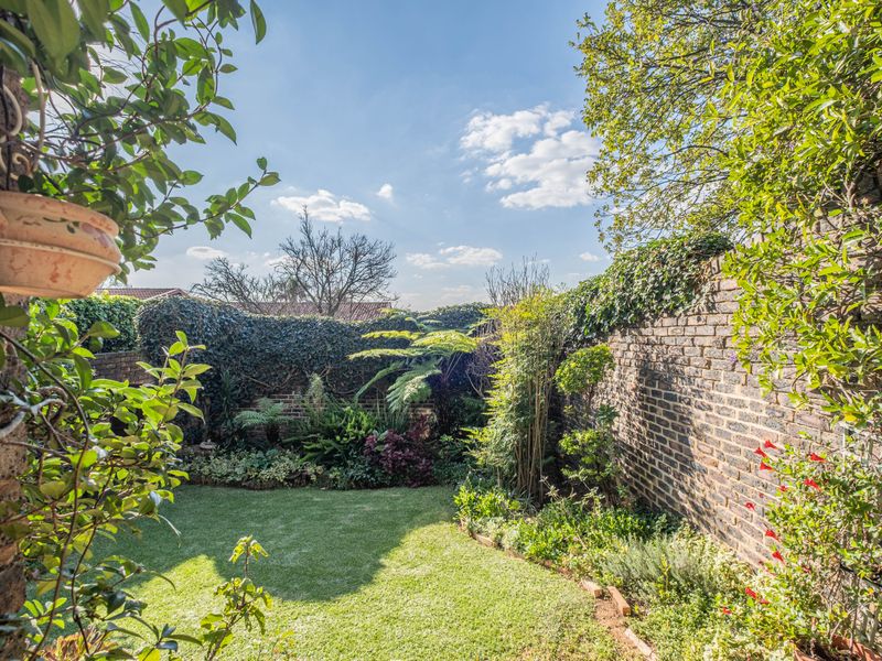 A well-maintained private garden featuring a lush lawn, established landscaped beds, and high brick boundary walls providing excellent privacy.