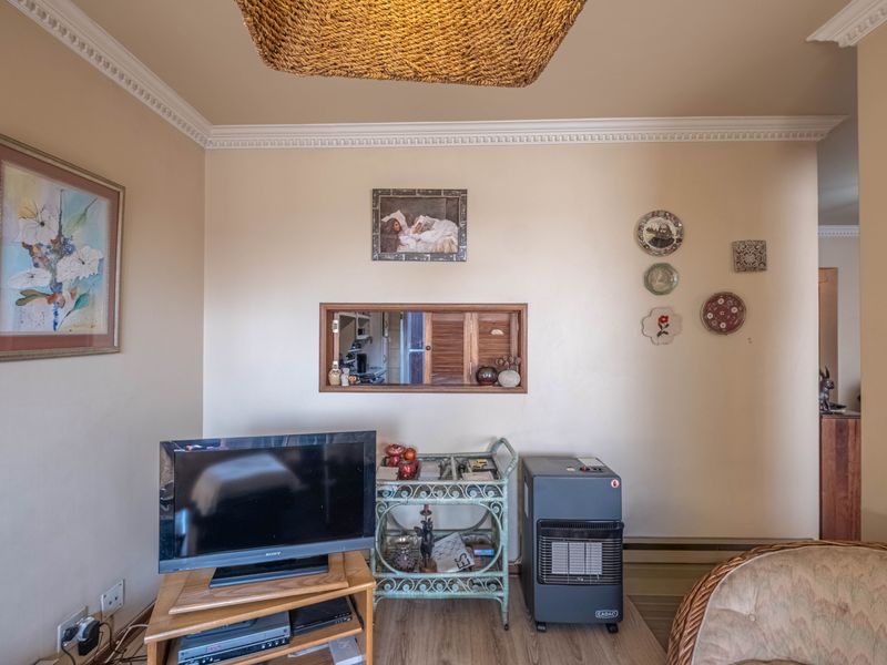 A living room featuring crown molding, laminate flooring, and a decorative pass-through window connecting to an adjacent space.