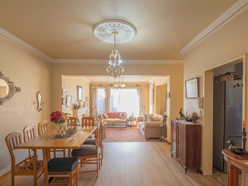 Spacious open-plan living and dining area featuring crown molding, a decorative ceiling rose, and light-toned laminate flooring, creating a warm and inviting atmosphere.