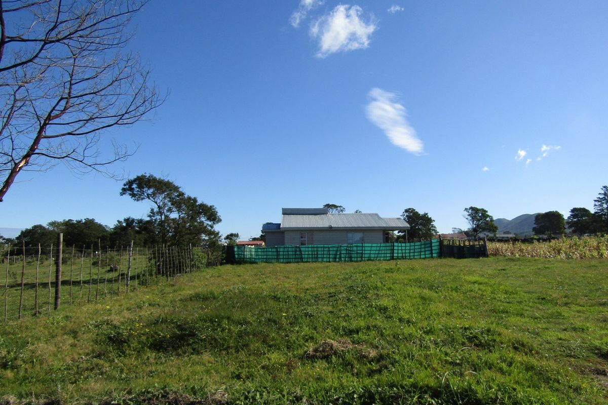 A view of the rear of the property featuring a corrugated metal roof and basic wire fencing with green privacy screening.
