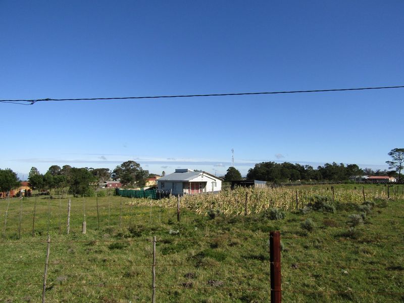 A distant view of a rural residential property featuring a simple structure with a metal roof, set within a large open field.