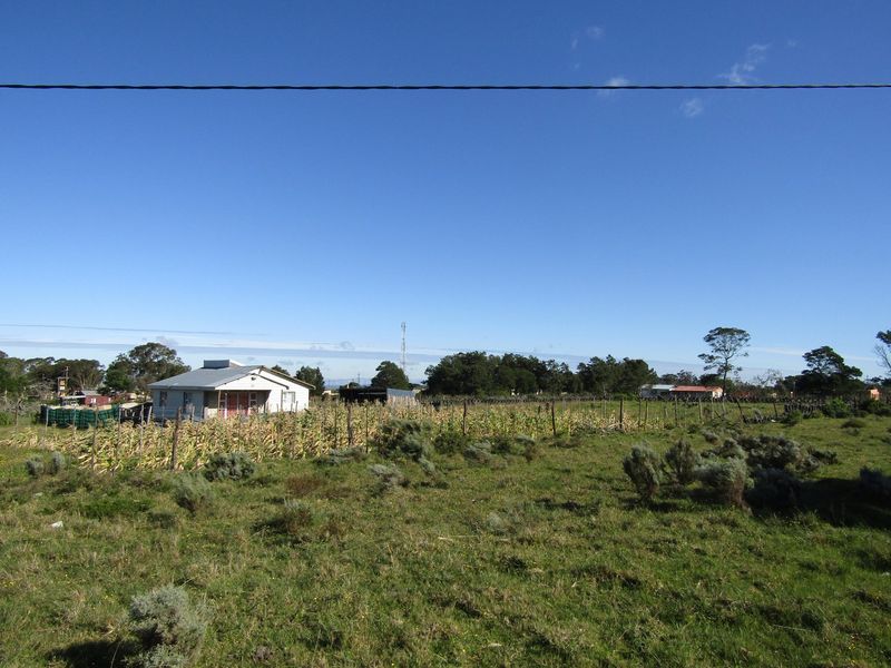 A wide-angle view of a rural property featuring a small dwelling with a metal roof, surrounded by open fields and wire fencing.