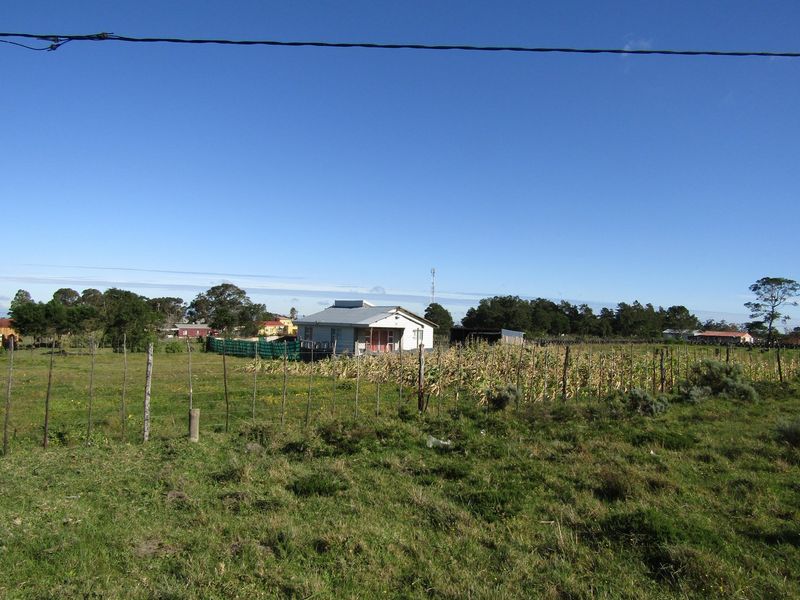 A distant view of a single-story house with a metal roof, situated on a large plot of land with a wire fence.