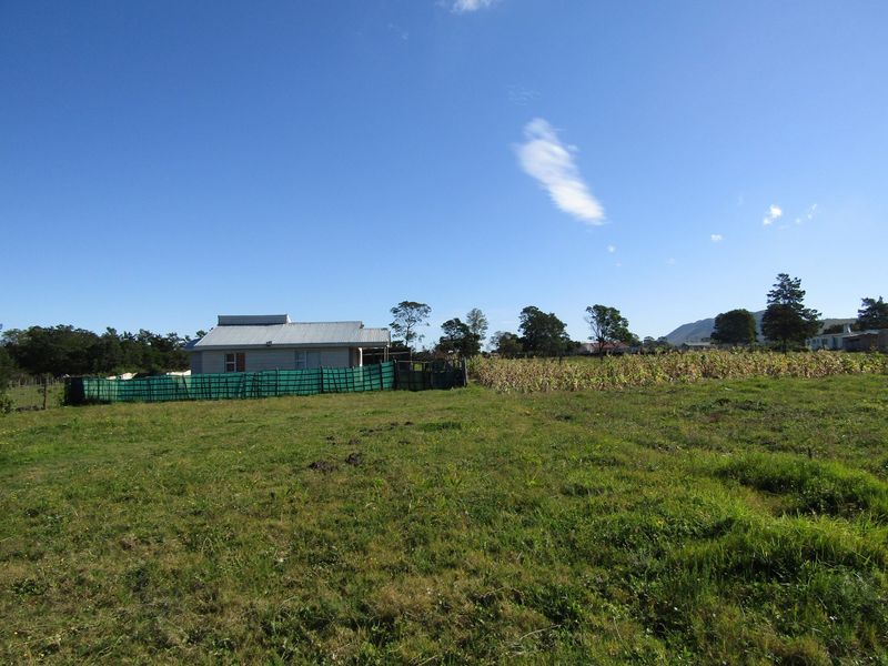 A view of a rural property featuring a small dwelling with a corrugated metal roof, surrounded by open fields and agricultural land.