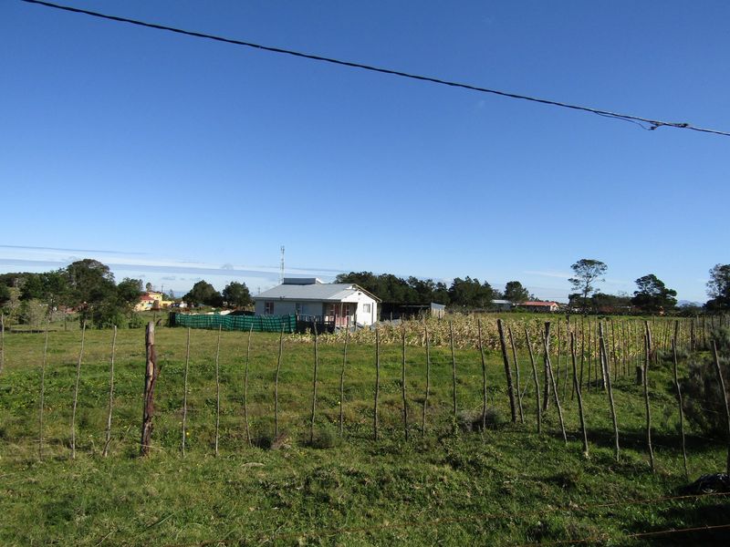 A detached residential house situated on a large rural plot, featuring a corrugated metal roof and a simple wooden perimeter fence.