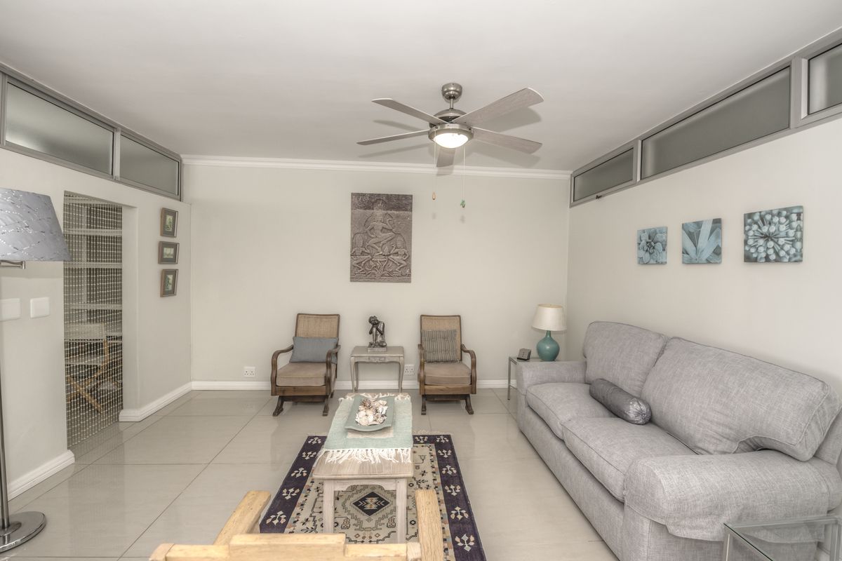A well-lit living room featuring neutral tiled flooring, a central ceiling fan, and high-level clerestory windows providing natural light.