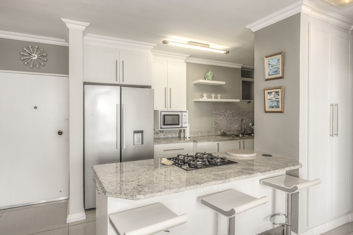 Modern kitchen featuring granite countertops, a built-in gas hob, ample cabinetry, and a functional breakfast bar layout.