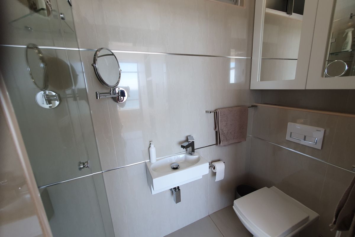Modern bathroom featuring a wall-hung toilet with concealed cistern, wall-mounted basin, and a glass-enclosed shower with neutral wall tiling.