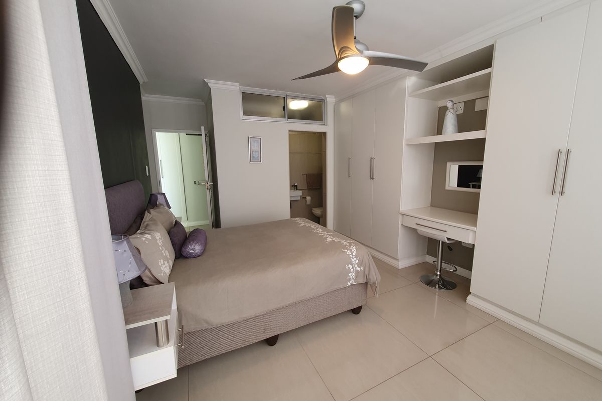 A well-maintained bedroom featuring extensive built-in cabinetry, a dedicated vanity area, modern tiled flooring, and an integrated ceiling fan with en-suite access.