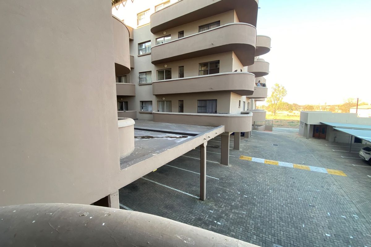 Exterior view of the apartment building showing the rear facade, paved parking area, and multiple balconies.