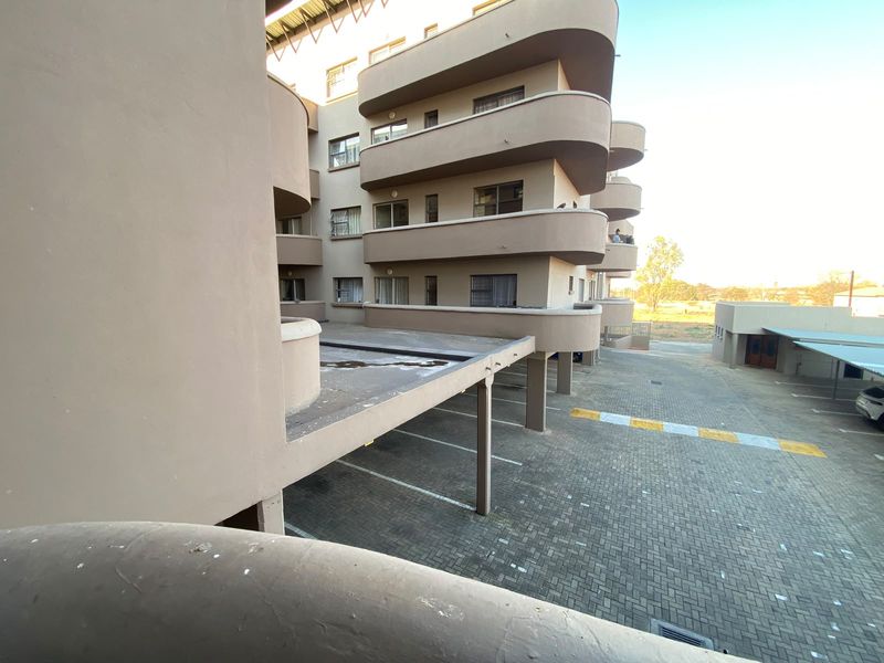 Exterior view of the apartment building showing the rear facade, paved parking area, and multiple balconies.