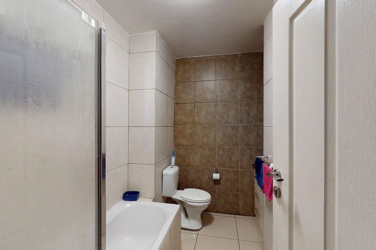 A functional bathroom featuring a bathtub, shower screen, toilet, and tiled finishes throughout.