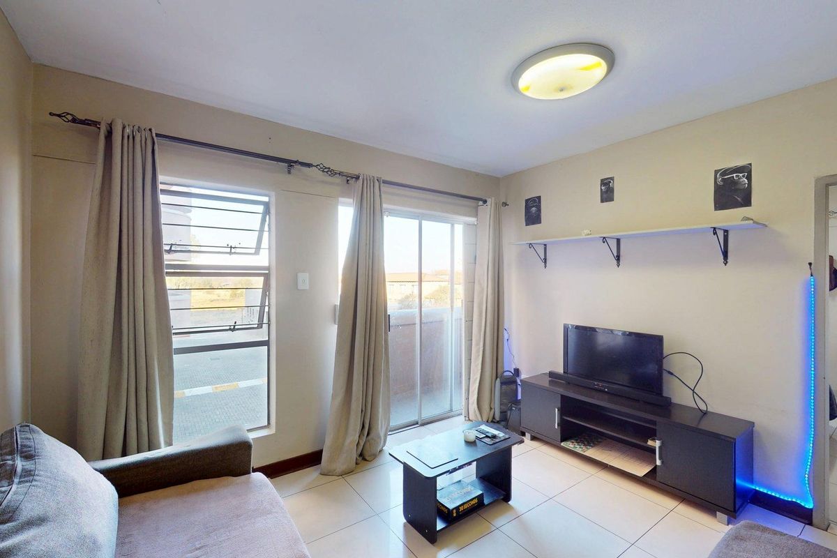 A living room featuring tiled flooring, a sliding glass door leading to a balcony, and wall-mounted shelving.