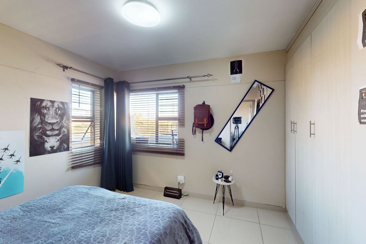 A bedroom featuring tiled flooring, built-in cupboards, and dual windows with venetian blinds and curtain rods.