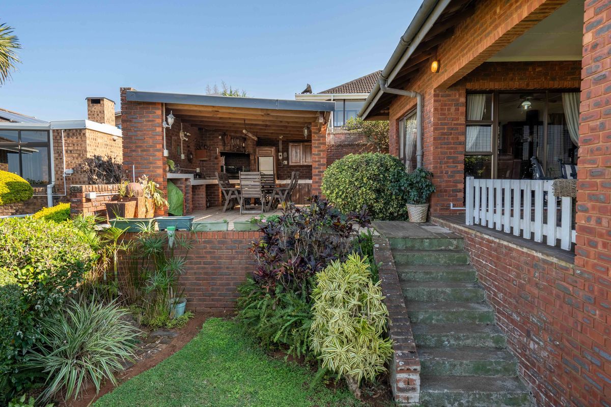 Rear exterior view featuring a covered brick patio with a built-in braai, accessible via brick stairs from the garden area.