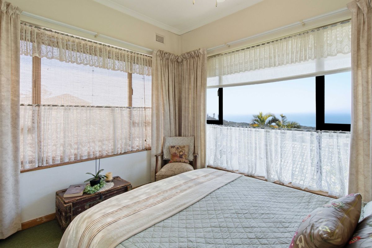A bright bedroom featuring corner windows with ocean views, neutral wall finishes, and carpeted flooring.