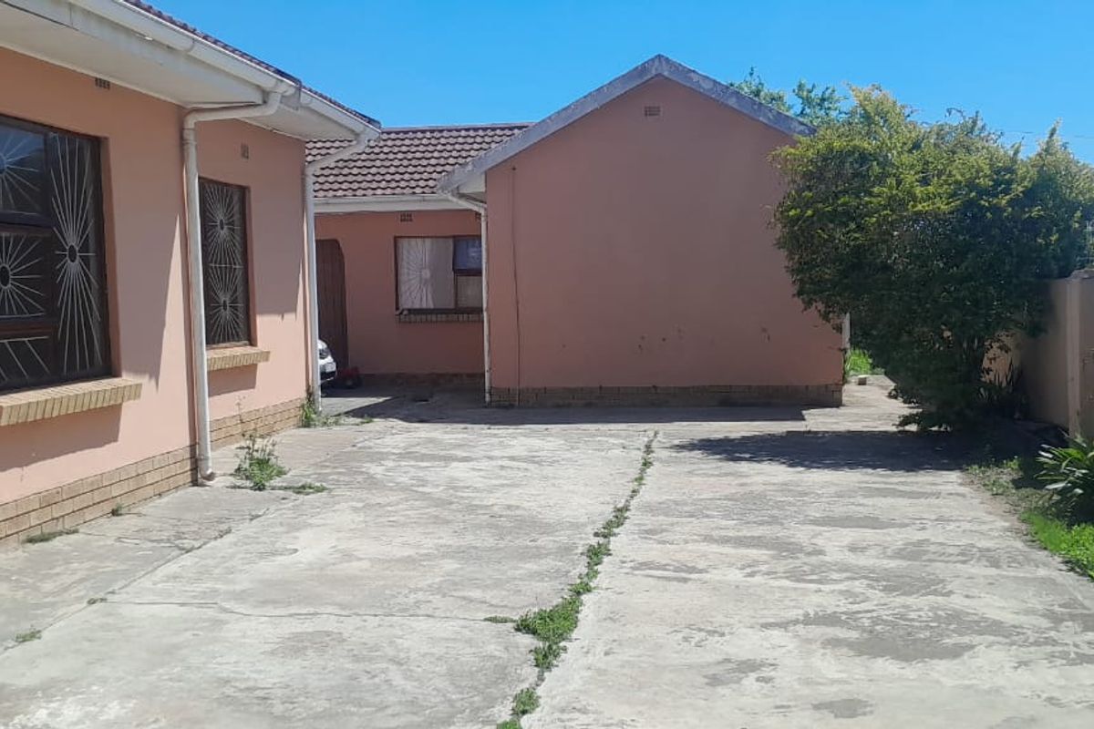 Rear exterior view of the property featuring a concrete driveway, perimeter wall with security fencing, and tiled roof structures.
