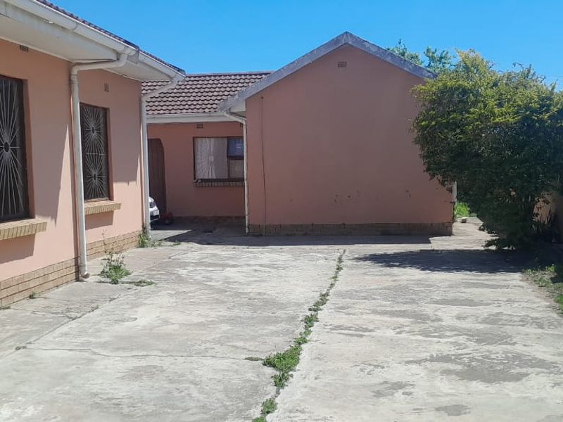 Rear exterior view of the property featuring a concrete driveway, perimeter wall with security fencing, and tiled roof structures.