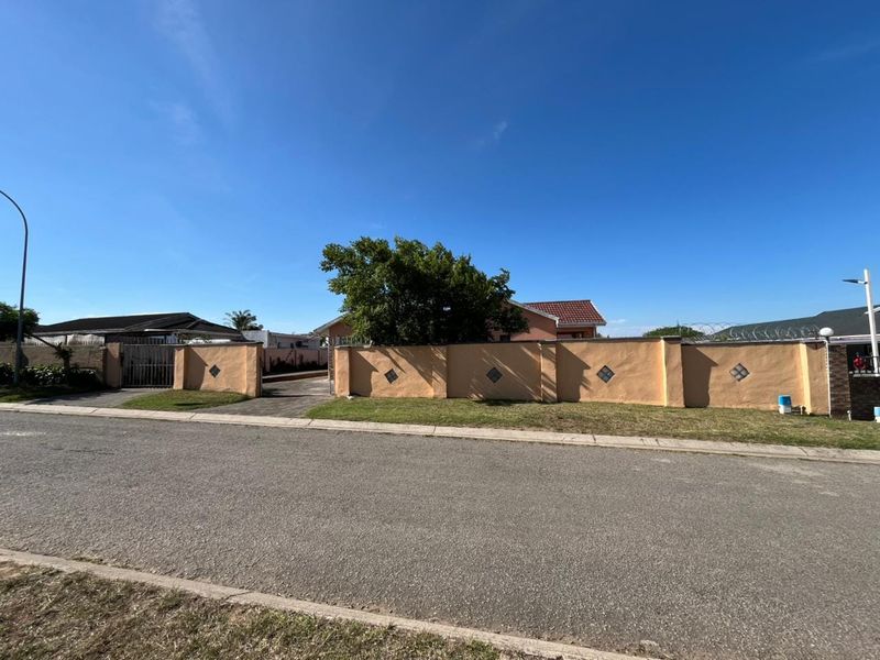 Street view of the property showing the front perimeter wall, gated driveway entrance, and established landscaping.
