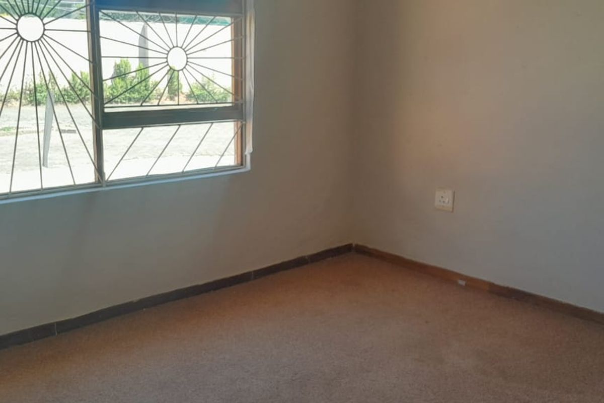 An empty bedroom featuring carpet flooring and a window fitted with security bars, offering a blank canvas for potential updates.