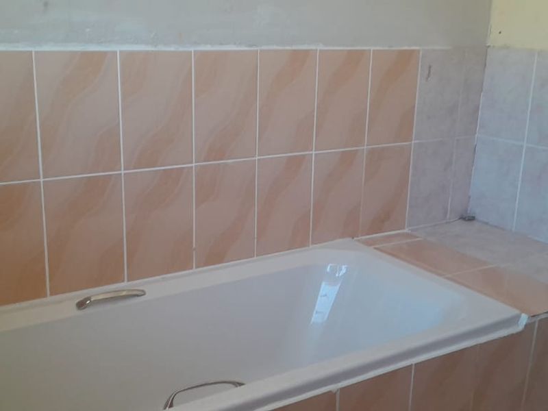 A bathroom featuring a built-in bathtub with tiled surround and splashback, currently requiring finishing work on the surrounding walls.