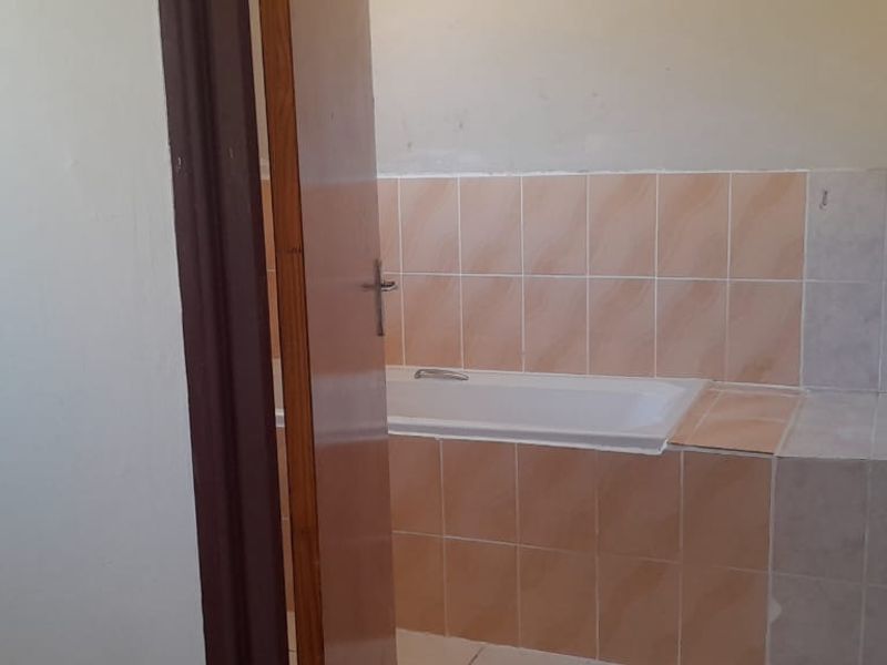 A view into a bathroom featuring a built-in bathtub with peach-toned wall tiling.