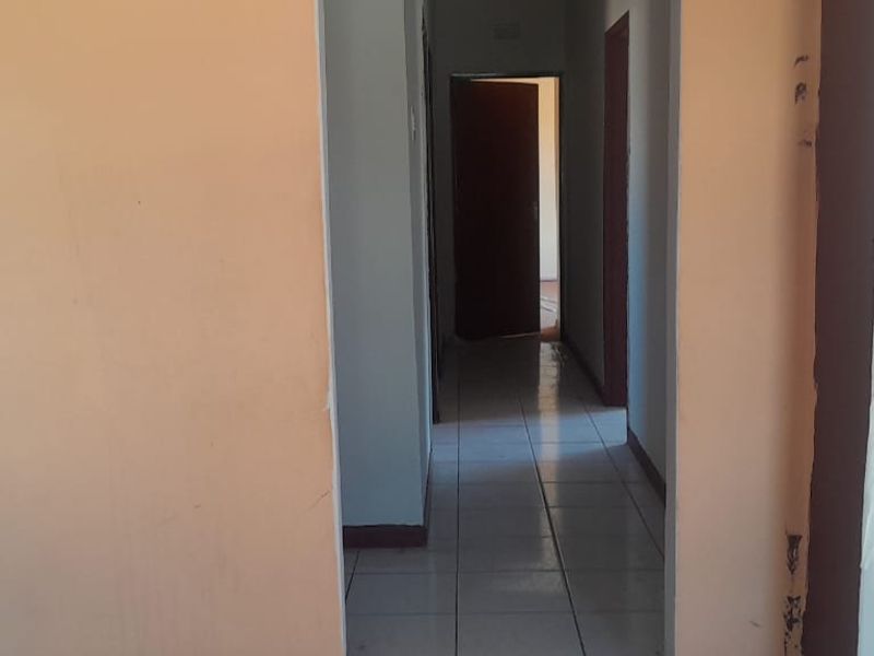 A vacant hallway featuring tiled flooring and access to multiple internal rooms, showing signs of wear on the walls and door frames.