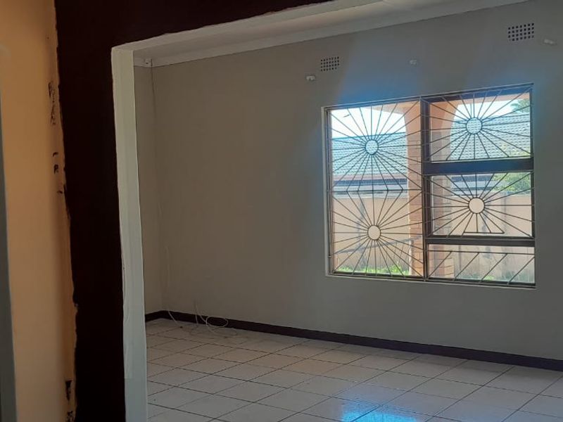 An empty living area featuring tiled flooring, security bars on windows, and unfinished wall paint, offering a blank canvas for renovation.