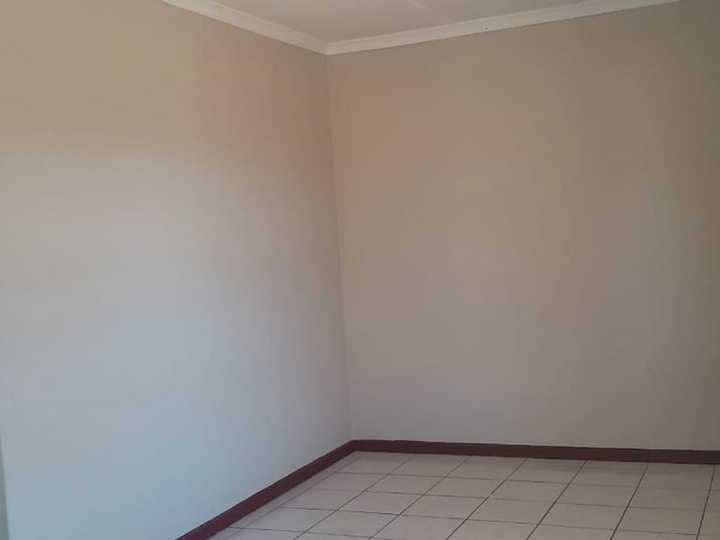 A bright, empty living room featuring neutral wall paint, tiled flooring, and a security gate on the window.