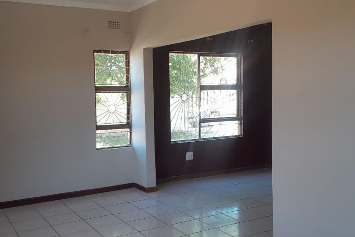 An empty, open-plan living area featuring tiled flooring and large windows fitted with security bars, offering a neutral canvas for interior design.