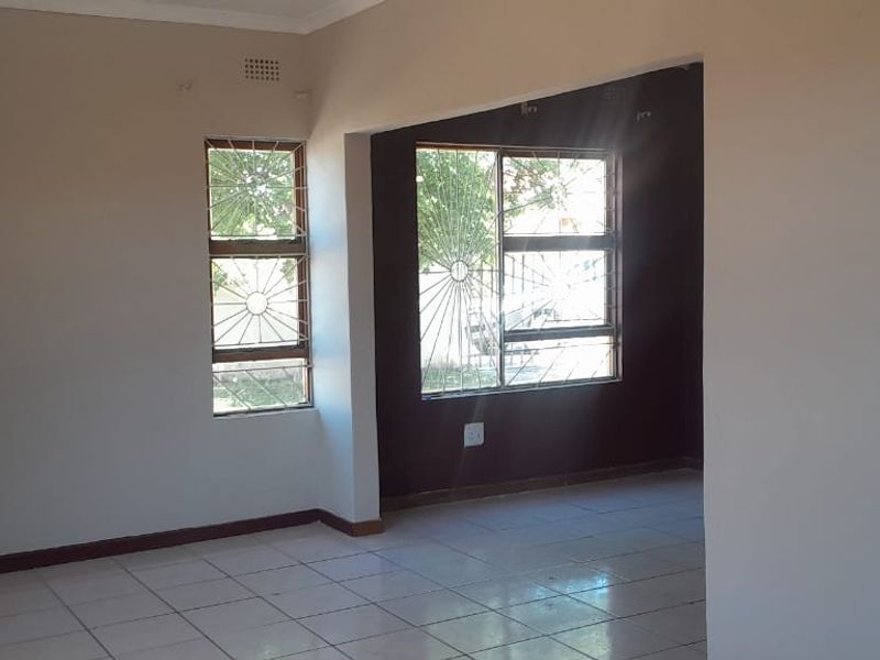 An empty, open-plan living area featuring tiled flooring and large windows fitted with security bars, offering a neutral canvas for interior design.