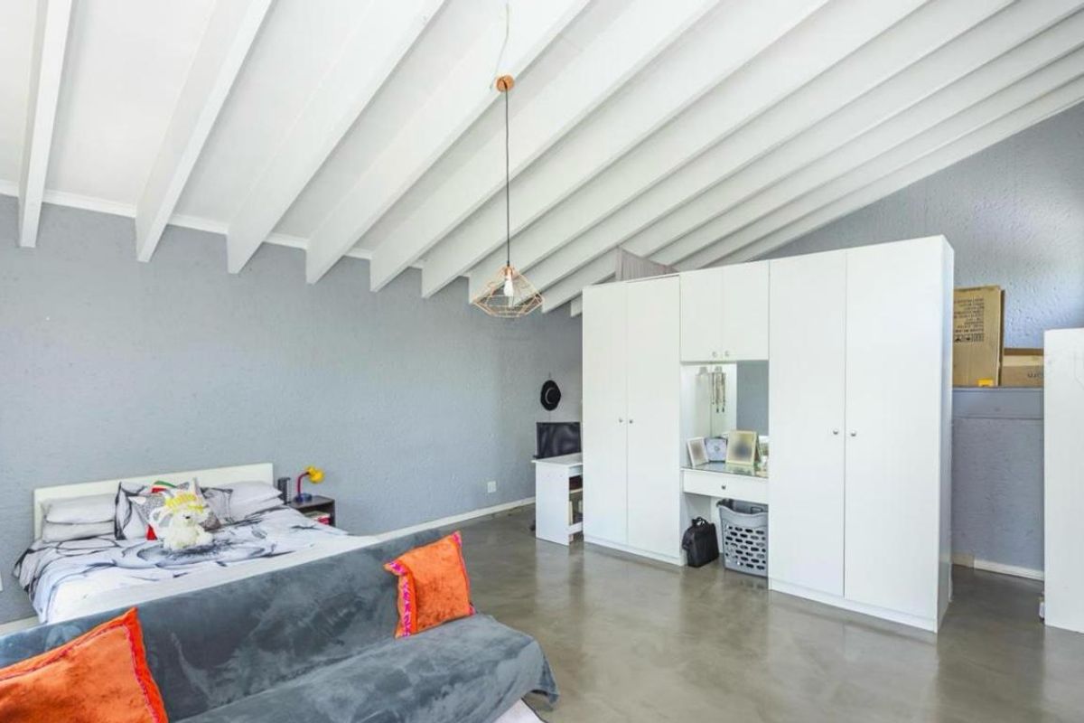 Spacious bedroom featuring high exposed beam ceilings, polished concrete flooring, and a large built-in wardrobe with integrated vanity.